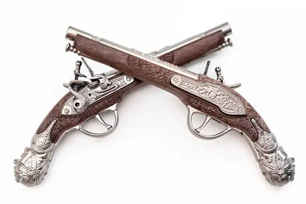 Firearms dating to the american revolution and antique collectables concept with ornate old fashioned dueling flintlock pistols crossed in duel isolated on white background with clipping path cutout