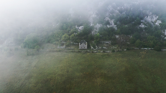 Aerial view of stone house without roof in mountains of Montenegro. Ruins, forest, fog, clouds. Grahovo