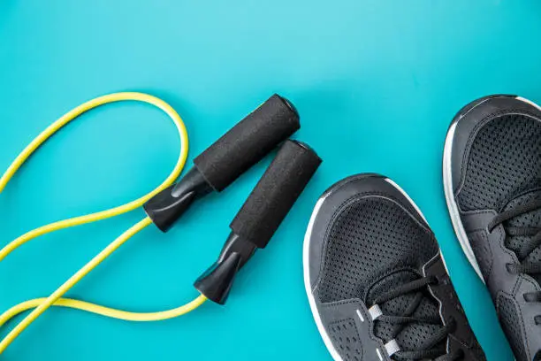 Black sport shoes and jump rope on colorful background. Top view.