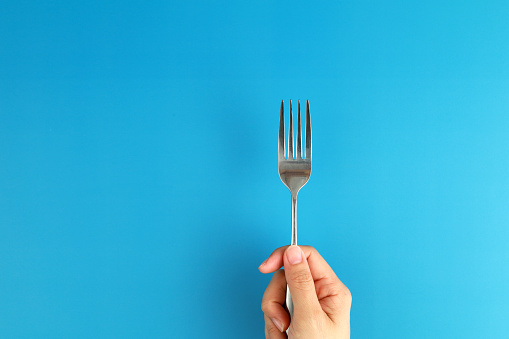 Female hand holding a fork on blue background