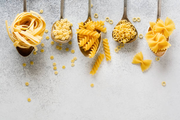 istock Various pasta in iron spoons on gray concrete background. Anellini pasta. Cooking concept. Top view. 1212107775