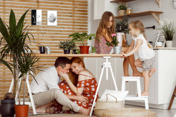 mom, dad and daughters are gaming near indoor flowers into a pot on the table in the kitchen of the house.
