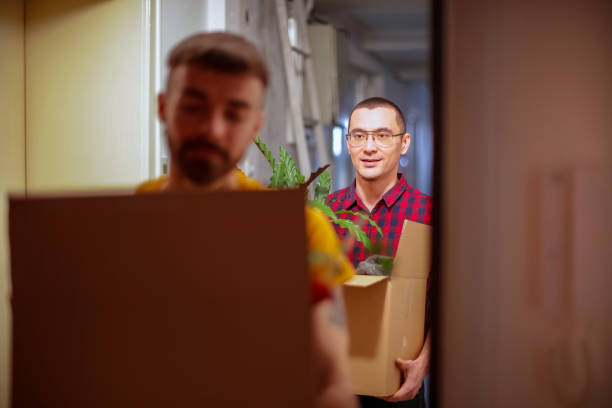 istock Walking behind his partner and carrying a box with houseplants in hallway 1212115628