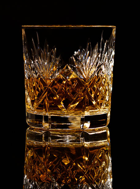 A crystal glass of whiskey with reflection against a black background.