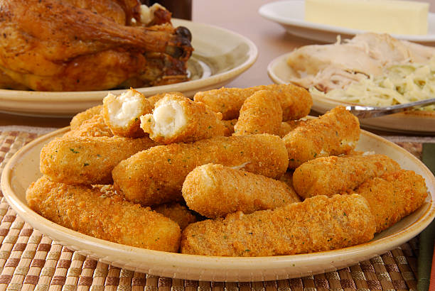 Breaded cheese sticks on a plate with table of food