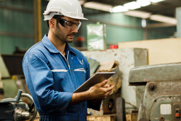 Maintenance engineer industrial plant with a tablet in hand and document plan, Engineer looking of working at industrial machinery setup in factory. stock photo