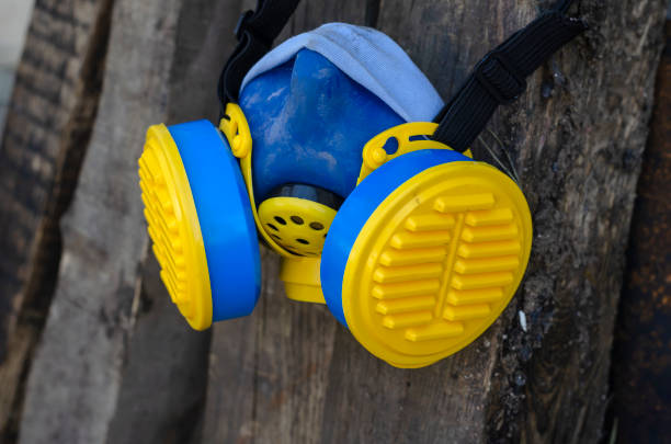 Used Respirator with filters. A yellow-blue respirator is hanging on a wooden beam. Personal protective equipment. Selective focus. Shooting outdoors. Close-up.