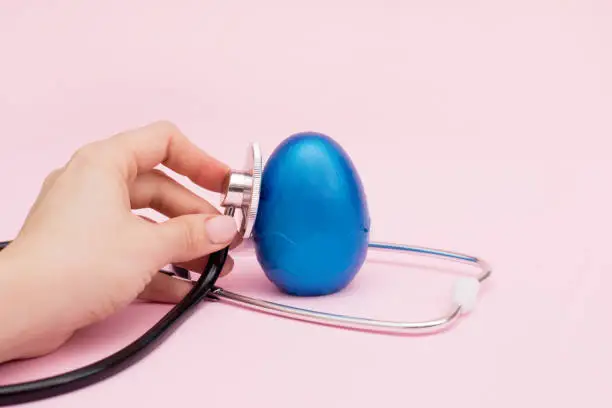 Stethoscope in doctor's hand with classic blue egg on a pink background. copy space, concept of medicine easter