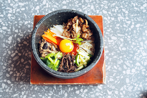 Korean mixed rice; made with steamed rice, vegetables, grilled pork and fried egg on top, served in a hot stone bowl. Selective focus.