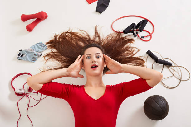 Horizontal picture of confused shocked female having surprised facial expression, putting hands on temples, opening mouth widely, choosing sport equipment, looking directly at camera. Choice concept. imagen horizontal de mujer confundida sorprendida que ha sorprendido la expresión facial, poniendo las manos en las sienes, abriendo la boca ampliamente, eligiendo equipo deportivo, mirando directamente a la cámara. concepto de elección.