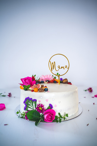 Sweet white cheesecake torte with fresh fruits and rose flowers on white wooden table background. Ideal gift for mother mama birthday, name-day and celebration.