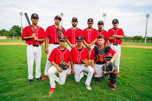 Portrait of teenage Hispanic baseball teammates suited up and standing outdoors with bat and gloves.
