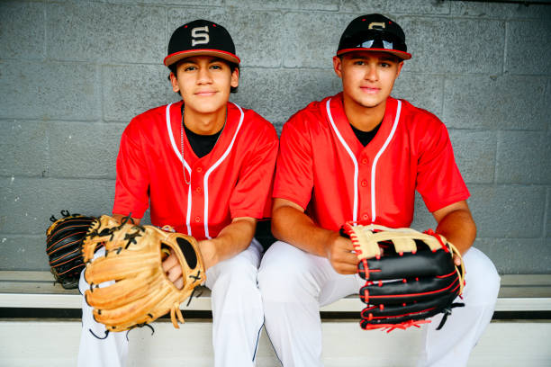 Portrait of Hispanic baseball players with gloves in dugout Close-up of young Hispanic baseball players with gloves sitting on bench in dugout and looking at camera. high school baseball stock pictures, royalty-free photos & images