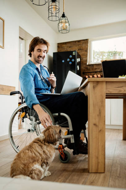 istock Happy disabled man cuddling his dog while working on laptop at home. 1212139589
