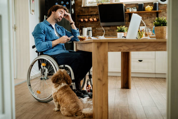 istock Exhausted businessman in wheelchair using cell phone while working at home. 1212140965