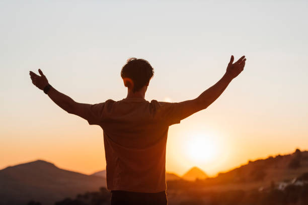 istock Rear view of man with arms outstretched at sunset 1212145995