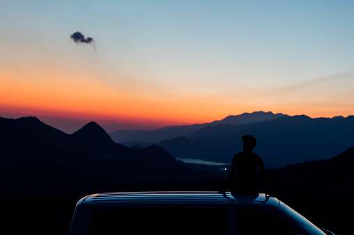Young man sitting on van enjoying the sunset, hillside, horizon, landscape