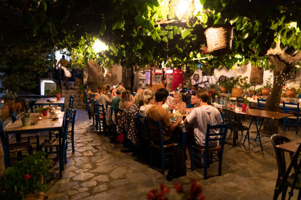 Group of friends eating dinner in Mediterranean courtyard Large group of friends sitting around table together enjoying al fresco dining in the evening outdoor dining photos stock pictures, royalty-free photos & images