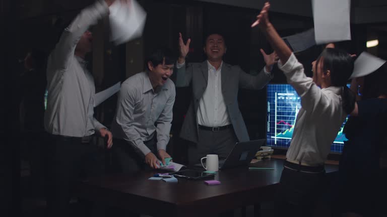 Businesspeople Asia throwing documents feeling happy of achievements after succeed result at meeting room at night office in city.