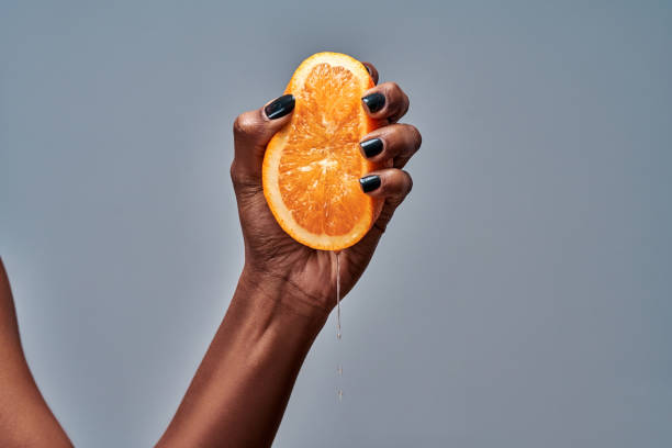 mano femenina apretando naranja aislada en gris - freshly squeezed fotografías e imágenes de stock