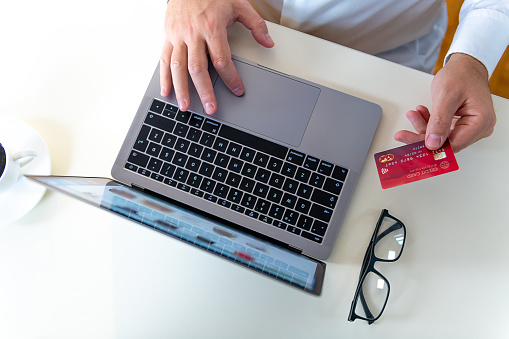 Closeup of caucasian hands interacting with a laptop and red credit card