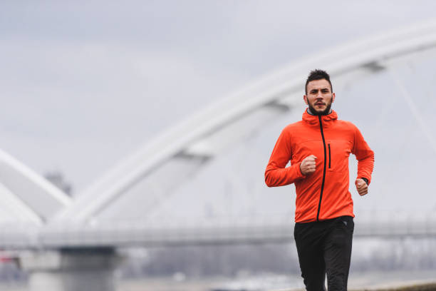 istock Handsome young athlete man running fast along river in orange windbreaker jacket 1212160003