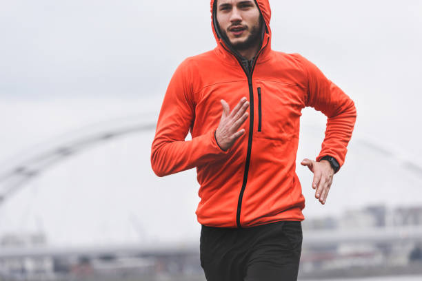 istock Handsome young athlete man running fast along river in orange windbreaker jacket 1212161289