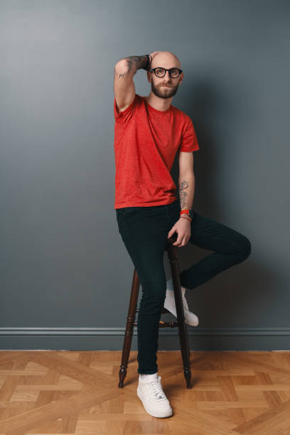 istock Stylish young man posing in the studio on gray background touching his hairless head while looking to camera 1212161651