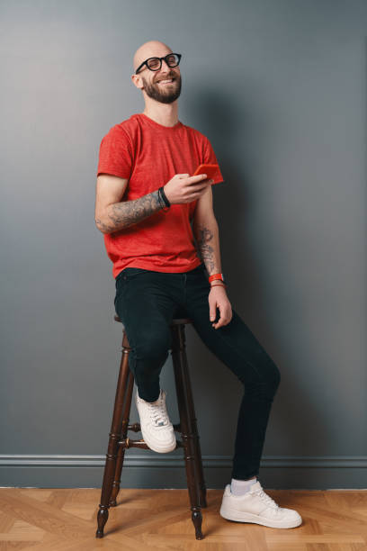 istock Handsome hairless man with beard,texting while holding smartphone in his tattooed arm on gray studio background 1212161666
