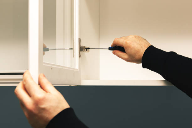 mestre ajusta a dobradiça da porta do armário da cozinha com uma chave de fenda - cabinet door - fotografias e filmes do acervo