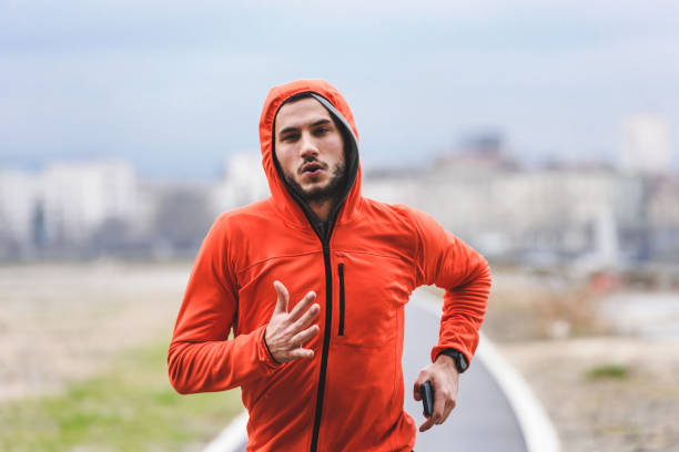 istock Handsome young athlete man running fast along river in orange windbreaker jacket 1212163520