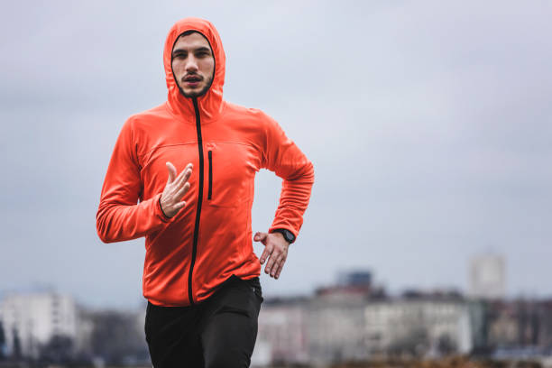 istock Handsome young athlete man running fast along river in orange windbreaker jacket 1212164488