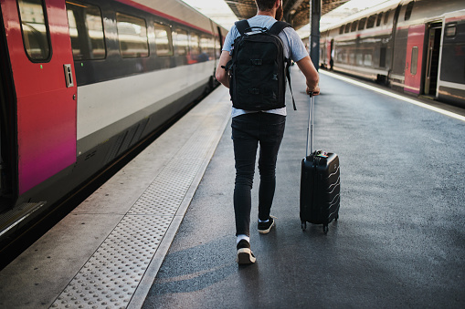 Shot of a young man heading towards the train with his luggage