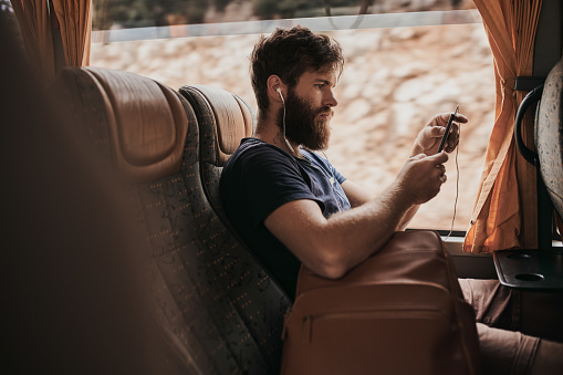 Shot of a man listening to music through his cellphone while sitting on the bus