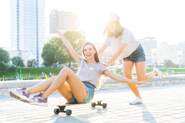 istock Two smiling young girls having fun while riding on a skateboard at the park. 1212165835