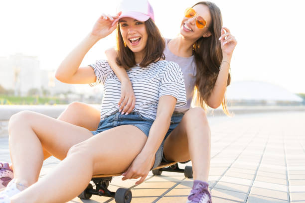 istock Two smiling young girls having fun while riding on a skateboard at the park. 1212166491