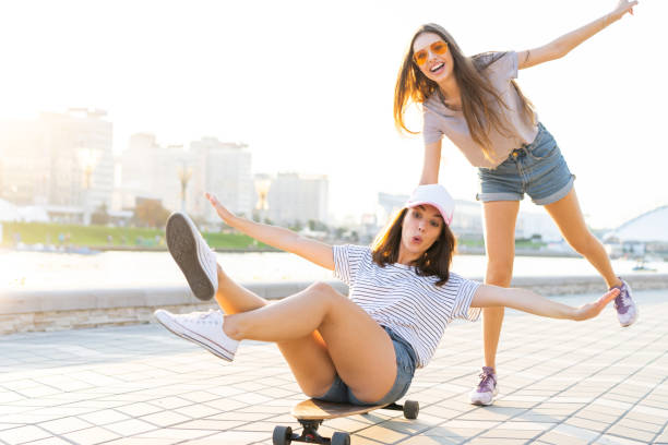 istock Two smiling young girls having fun while riding on a skateboard at the park. 1212166496