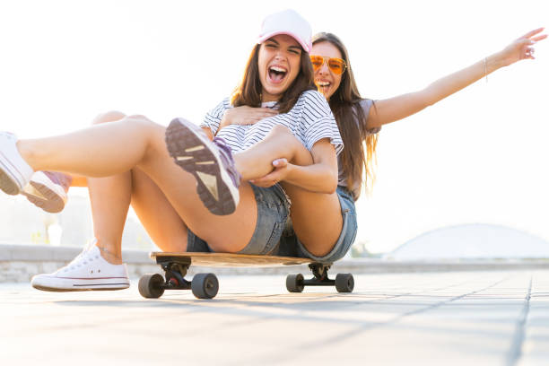 istock Two smiling young girls having fun while riding on a skateboard at the park. 1212166500