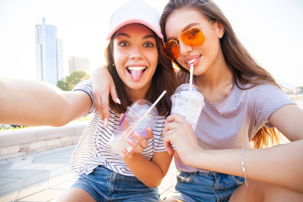istock Two smiling young girls having fun while sitting on a skateboard and taking a selfie at the park. 1212166607