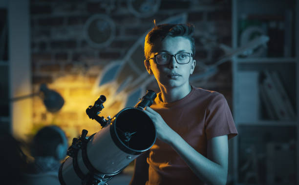 Smart boy using a telescope and watching stars Smart nerd guy with glasses watching stars with a telescope in his bedroom at night, science and childhood concept astronomer photos stock pictures, royalty-free photos & images