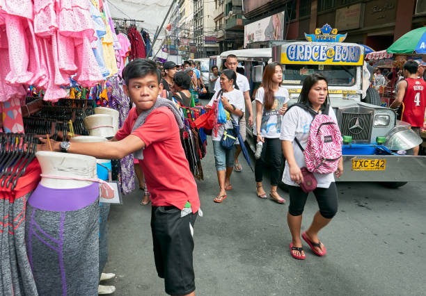 Crowd of shoppers walking in Divisoria Market Divisoria Market, Manila, Philippines - December 3, 2016: Young boy attending a clothing store, while shoppers walking next to a Philippine jeepney divisoria market stock pictures, royalty-free photos & images