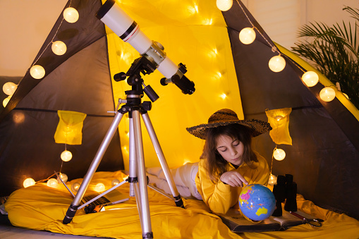Small girl using earth globe at home living room in a tent.