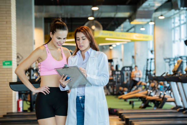 Sports medicine shows instructions to a woman athlete Sports medicine, working in a gym, is in charge of taking care of athletes, shows the instructions of a plan to follow an athlete sports medicine photos stock pictures, royalty-free photos & images