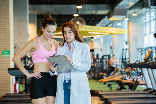Sports medicine shows instructions to a woman athlete Sports medicine, working in a gym, is in charge of taking care of athletes, shows the instructions of a plan to follow an athlete sports physical stock pictures, royalty-free photos & images