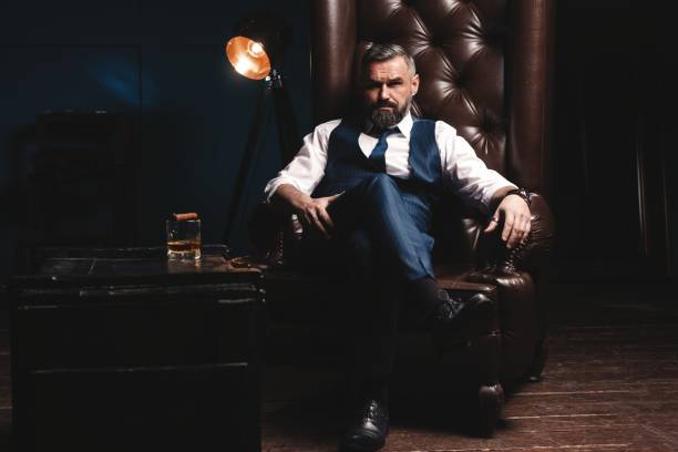 Attractive man with cigar and a glass whiskey Portrait of handsome elegant mature man with cigar and a glass whiskey in a dark room man cigar stock pictures, royalty-free photos & images