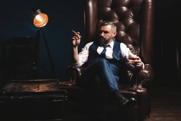 Attractive man with cigar and a glass whiskey Portrait of handsome elegant mature man with cigar and a glass whiskey in a dark room man cigar stock pictures, royalty-free photos & images