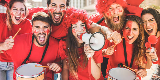 czerwoni fani sportu krzyczą, wspierając swoją drużynę ze stadionu - kibice piłki nożnej bawią się na zawodach - mistrzowie i zwycięska koncepcja - skup się na twarzy środkowej dziewczyny - drum beats zdjęcia i obrazy z banku zdjęć