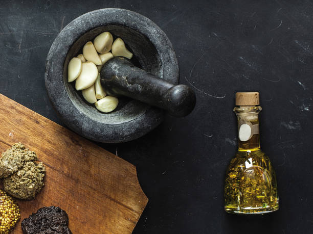 黒モルタルと害虫にニンニクの新鮮な部分が入っています。まな板にスパイスとソースとオリーブオイルのボトル。 - garlic cooking oil cutting board horizontal ストックフォトと画像