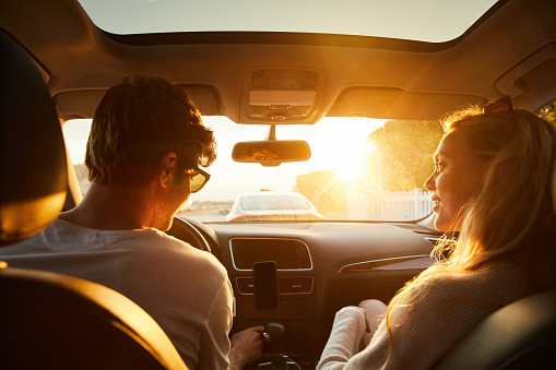 Rearview of a smiling young couple going on a road trip together in their car on a late summer afternoon
