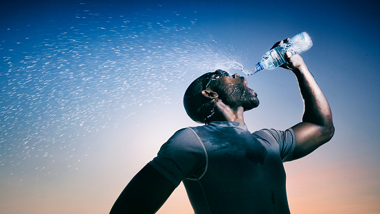 Close up of a young man drinking water from a plastic bottle underneath a clear sky.